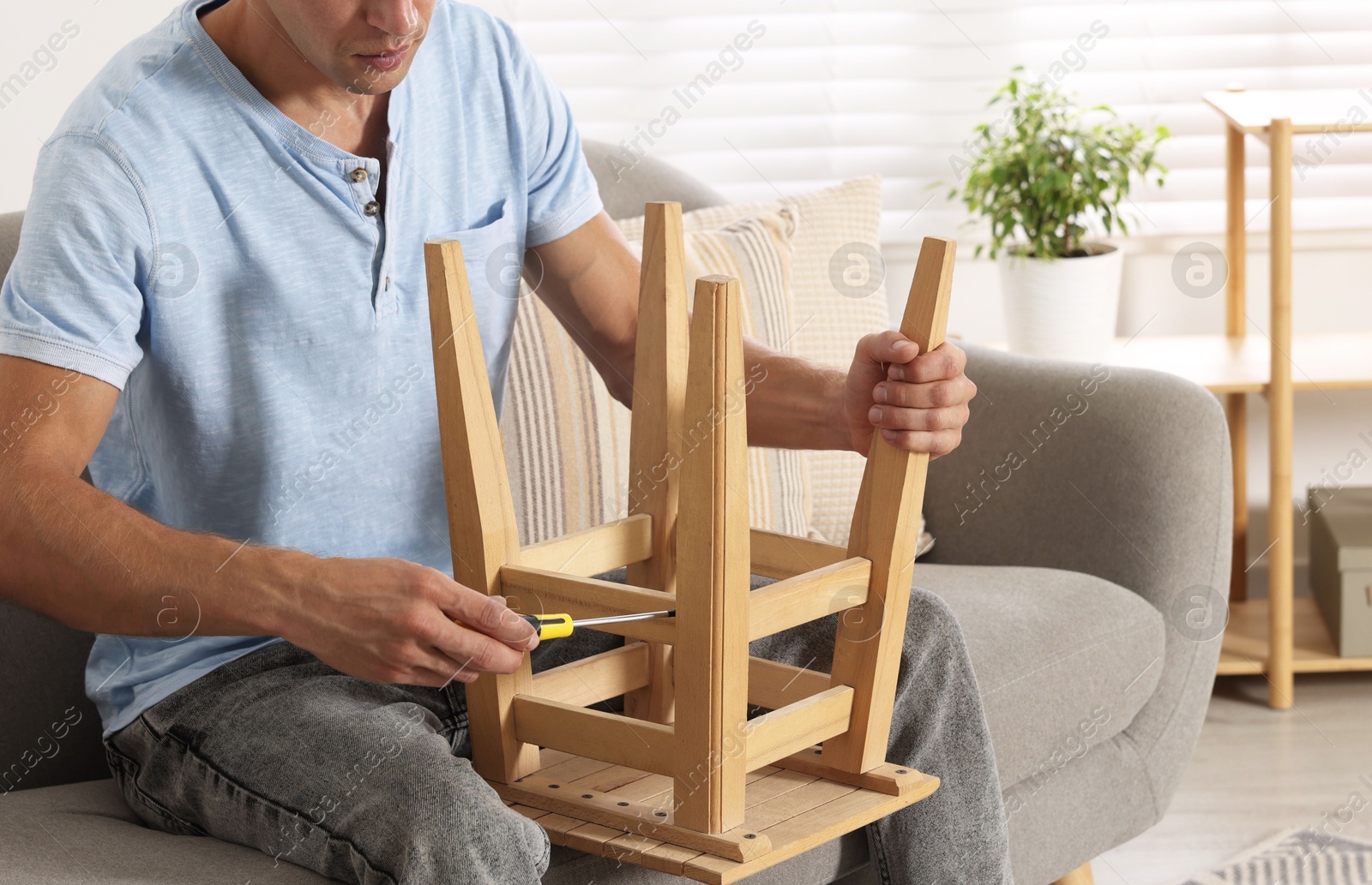 Photo of Man repairing wooden stool with screwdriver indoors, closeup