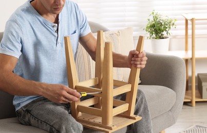 Photo of Man repairing wooden stool with screwdriver indoors, closeup