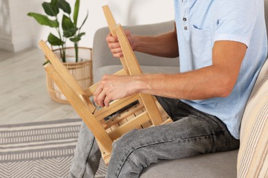 Photo of Man repairing wooden stool with screwdriver indoors, closeup