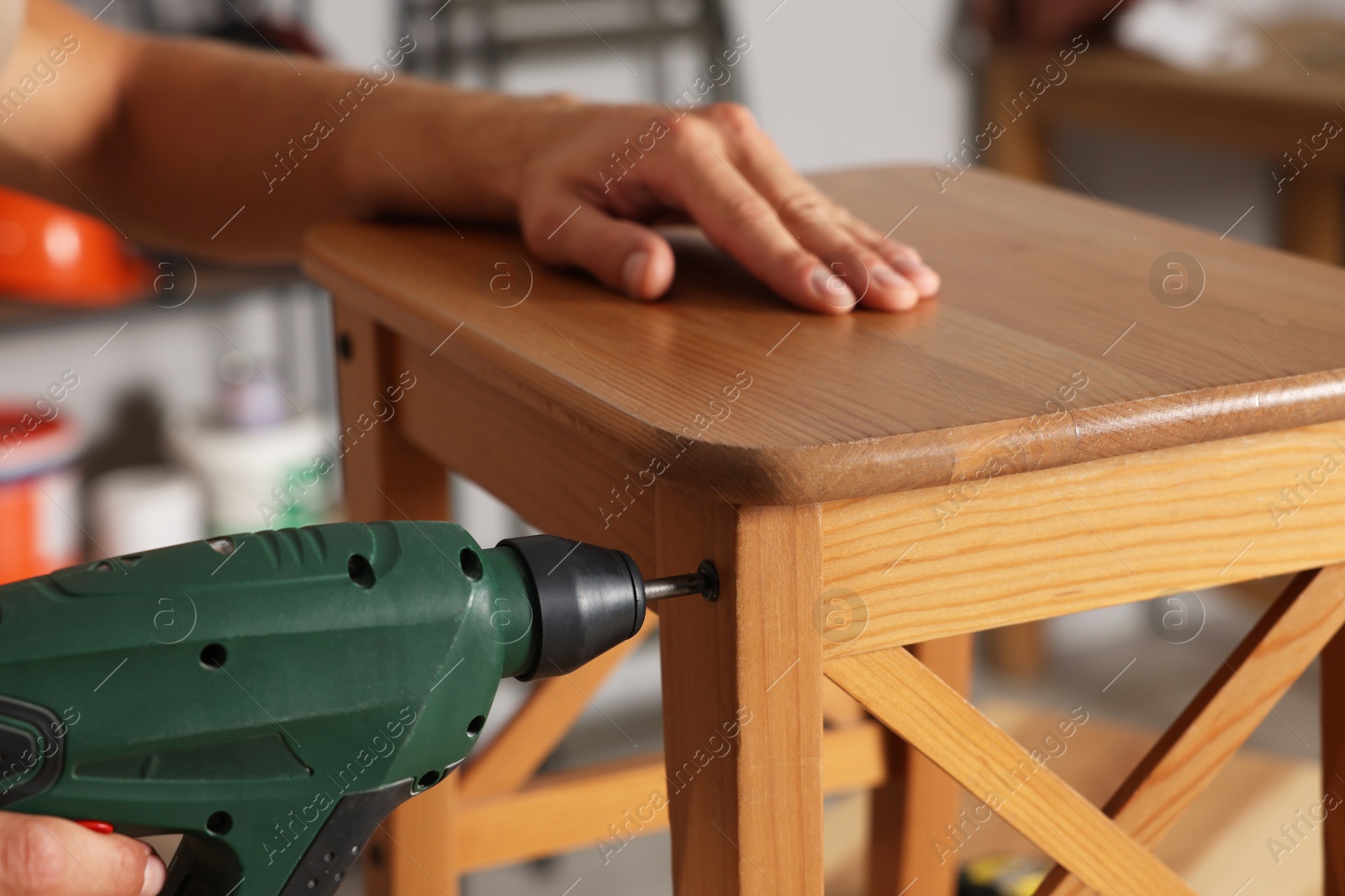 Photo of Man repairing wooden stool with electric screwdriver indoors, closeup