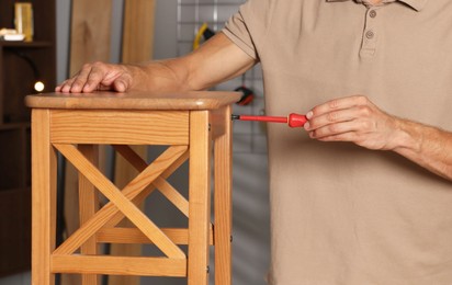 Man repairing wooden stool with screwdriver indoors, closeup