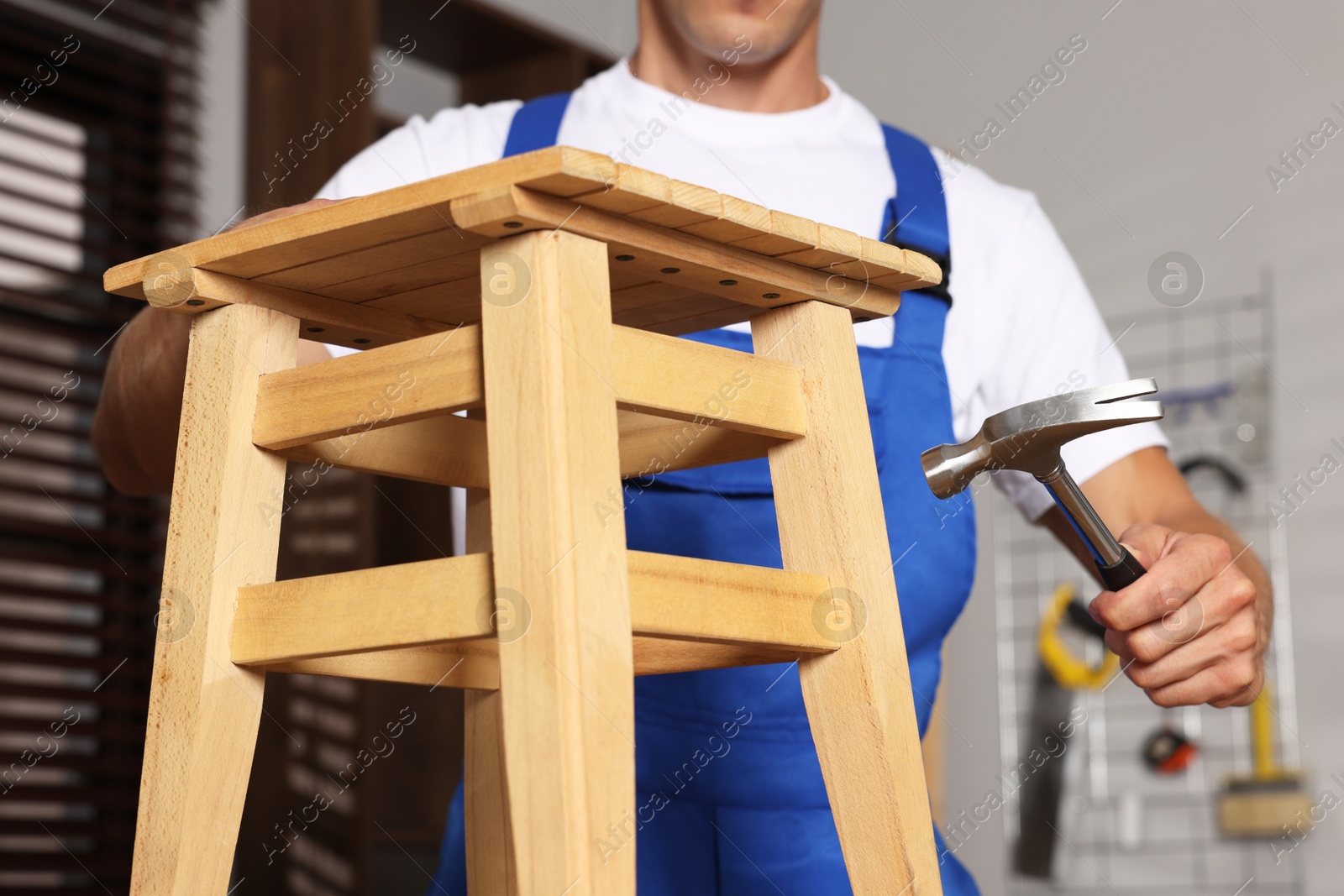 Photo of Man repairing wooden stool with hammer indoors, closeup