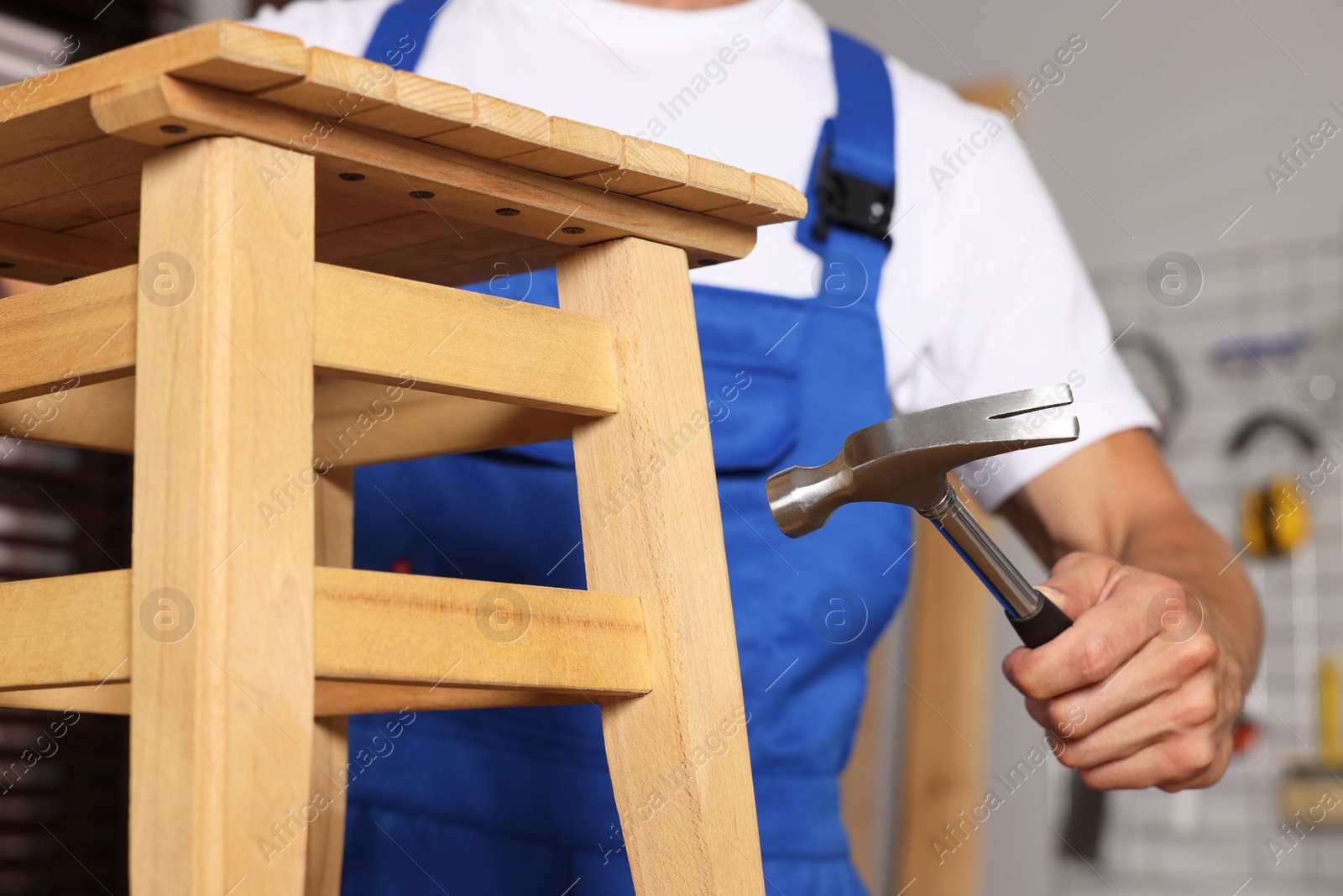 Photo of Man repairing wooden stool with hammer indoors, closeup