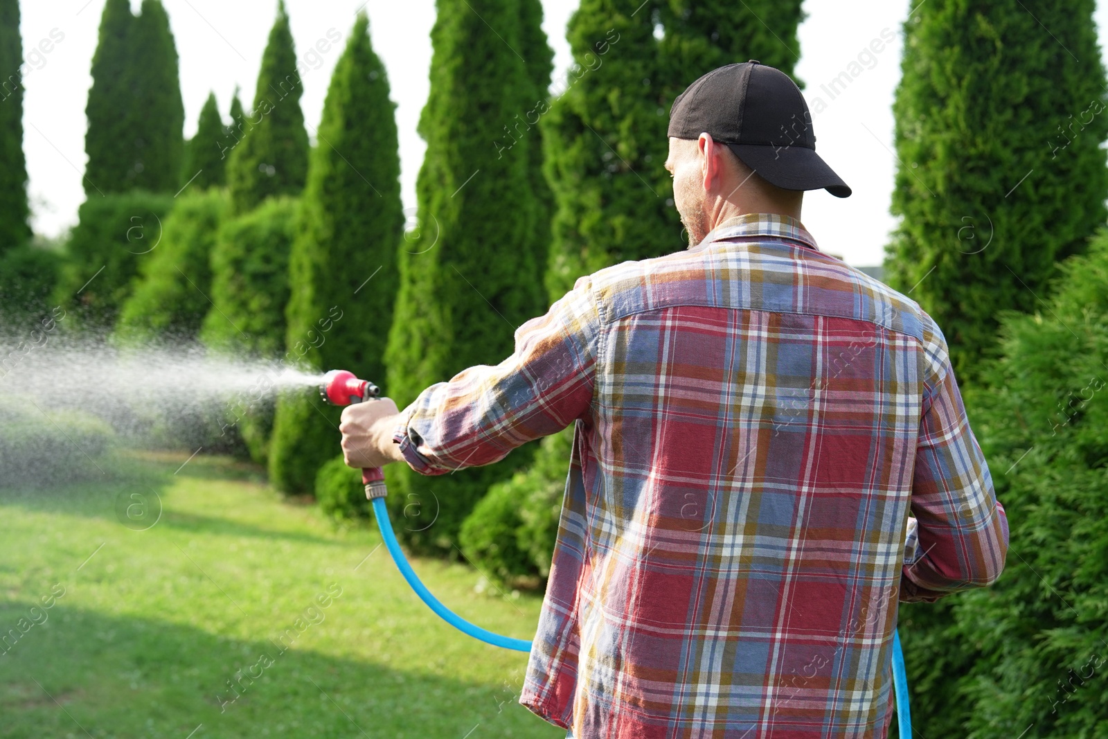 Photo of Man watering lawn with hose in backyard