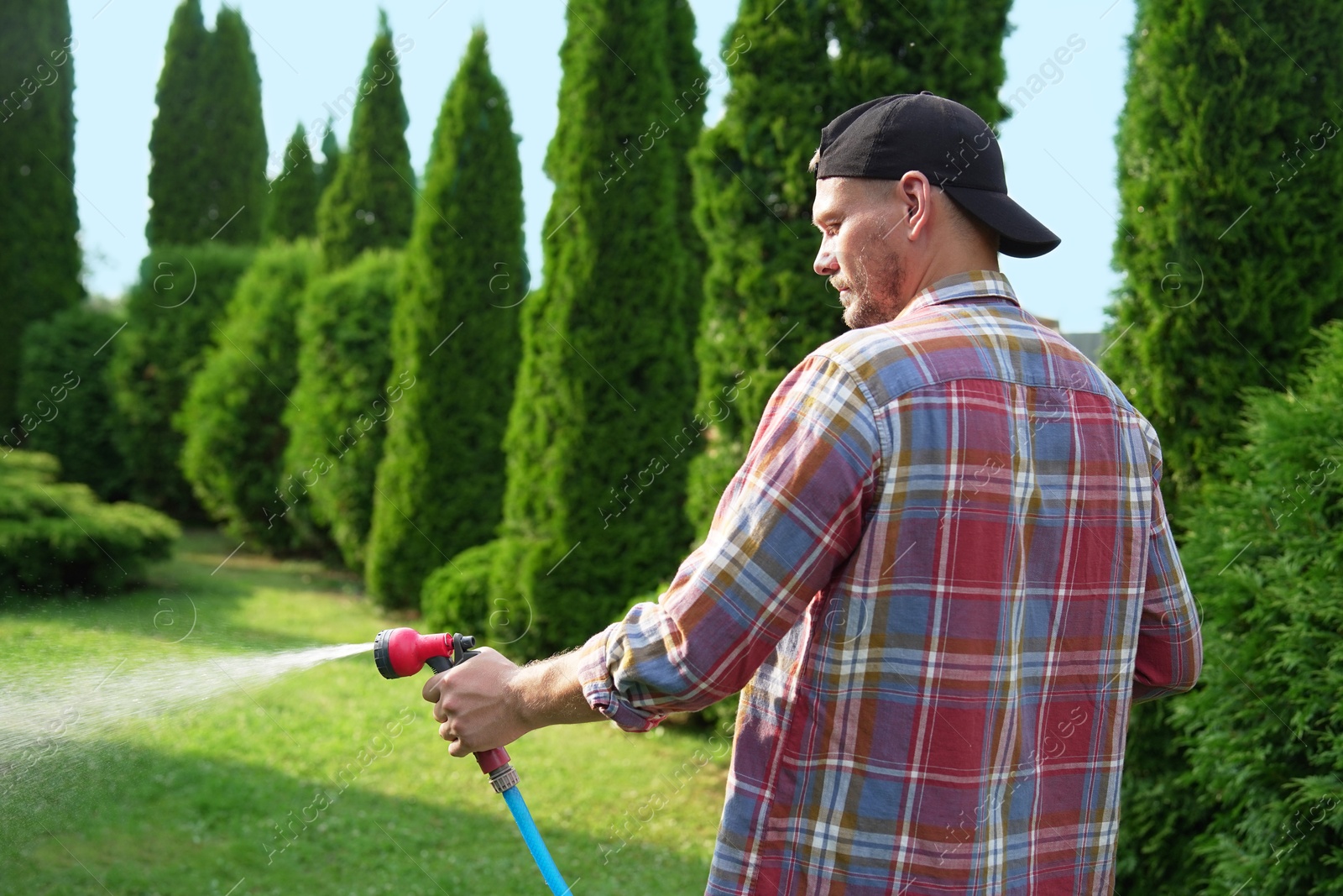 Photo of Man watering lawn with hose in backyard