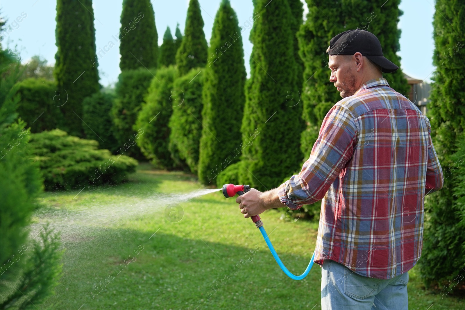 Photo of Man watering lawn with hose in backyard