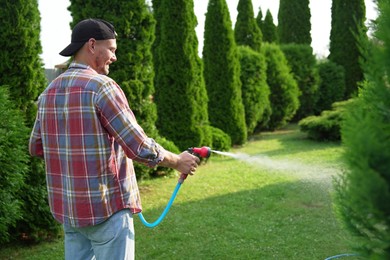 Man watering lawn with hose in backyard