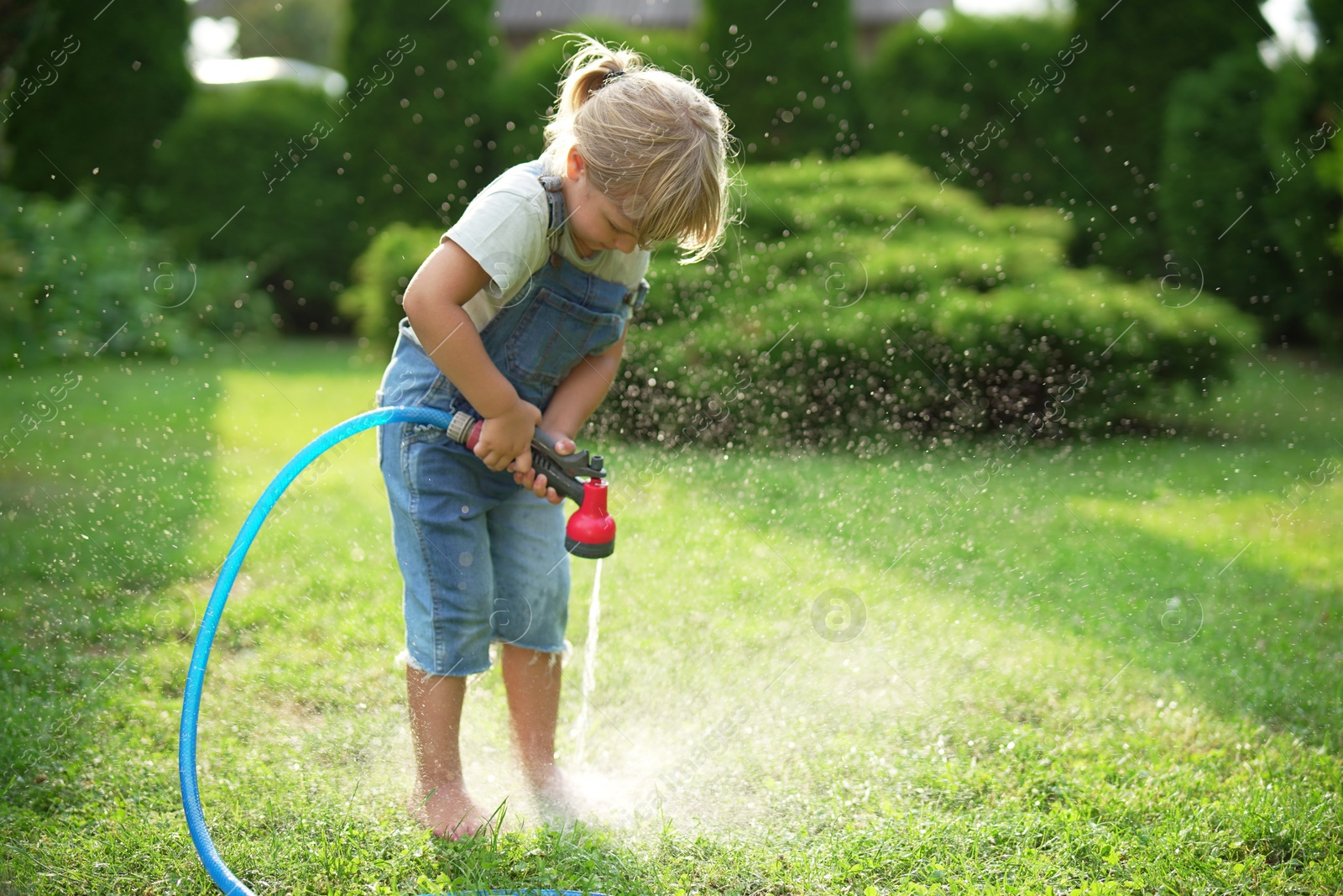 Photo of Little girl watering green grass on lawn in backyard