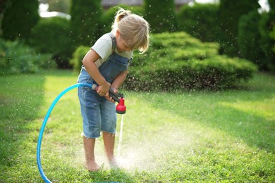 Little girl watering green grass on lawn in backyard