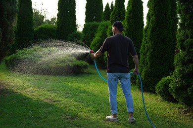 Man watering lawn with hose in backyard