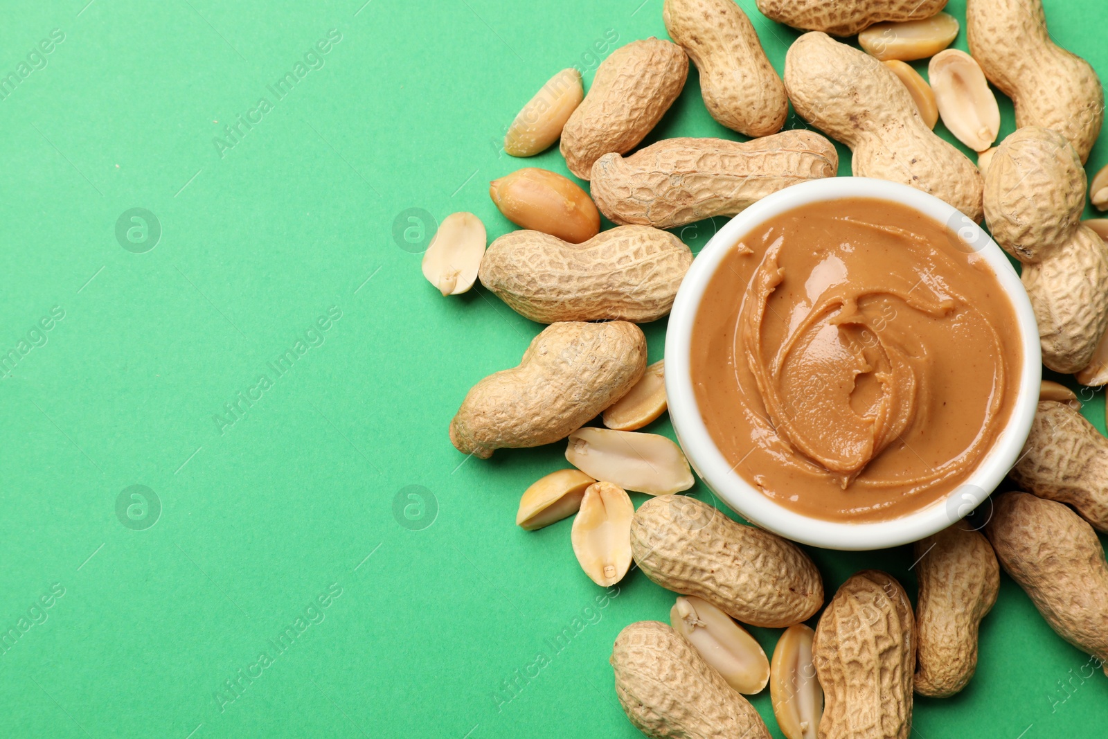 Photo of Tasty peanut butter in bowl and groundnuts on green background, flat lay. Space for text