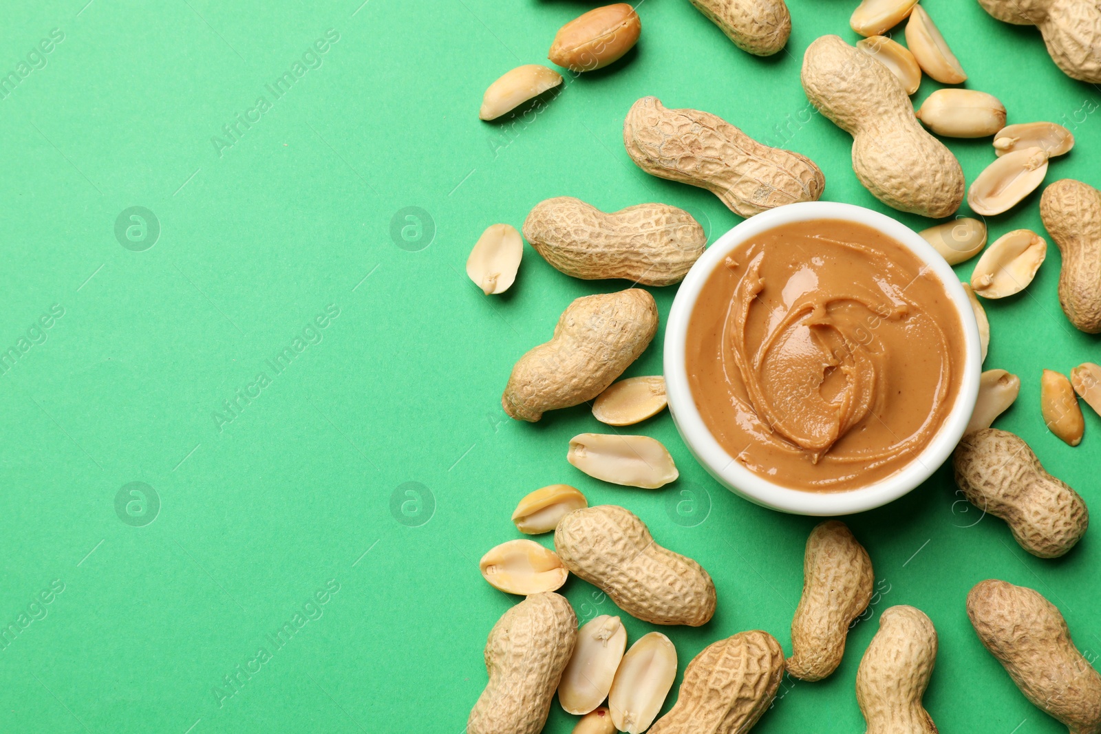 Photo of Tasty peanut butter in bowl and groundnuts on green background, flat lay. Space for text