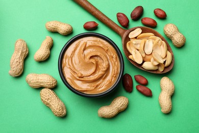 Photo of Tasty peanut butter and groundnuts on green background, flat lay