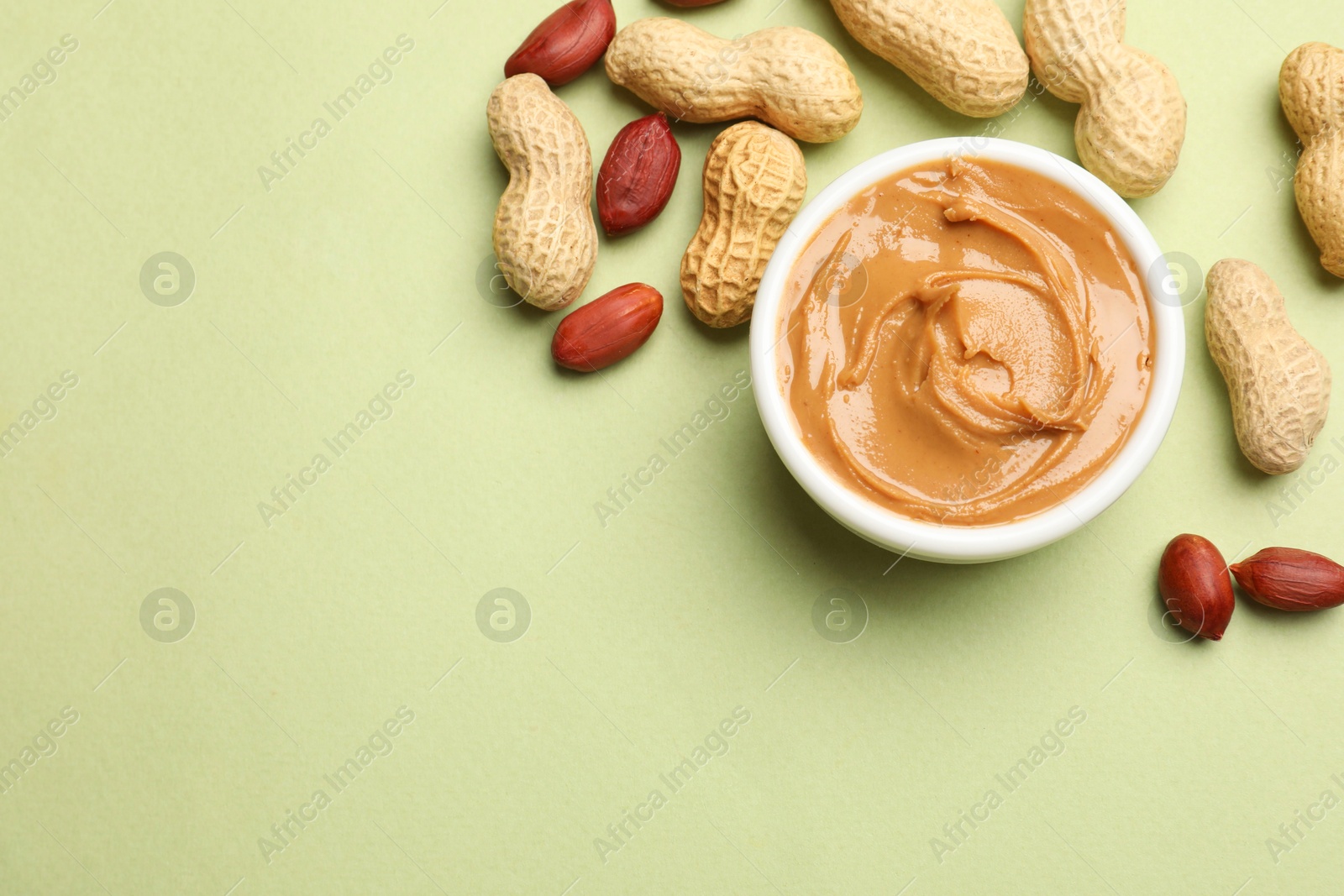 Photo of Tasty peanut butter in bowl and groundnuts on pistachio color background, flat lay. Space for text