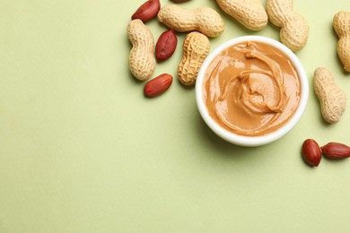 Tasty peanut butter in bowl and groundnuts on pistachio color background, flat lay. Space for text