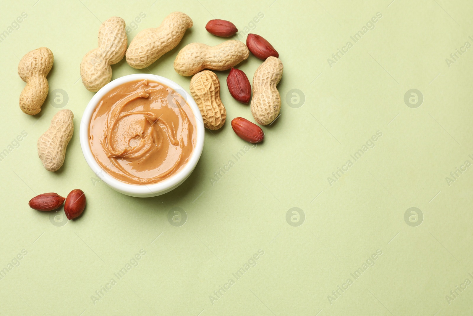 Photo of Tasty peanut butter in bowl and groundnuts on pistachio color background, flat lay. Space for text