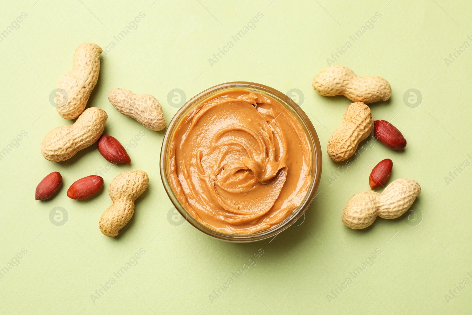 Photo of Tasty peanut butter in bowl and groundnuts on pistachio color background, flat lay