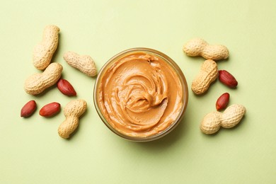 Tasty peanut butter in bowl and groundnuts on pistachio color background, flat lay