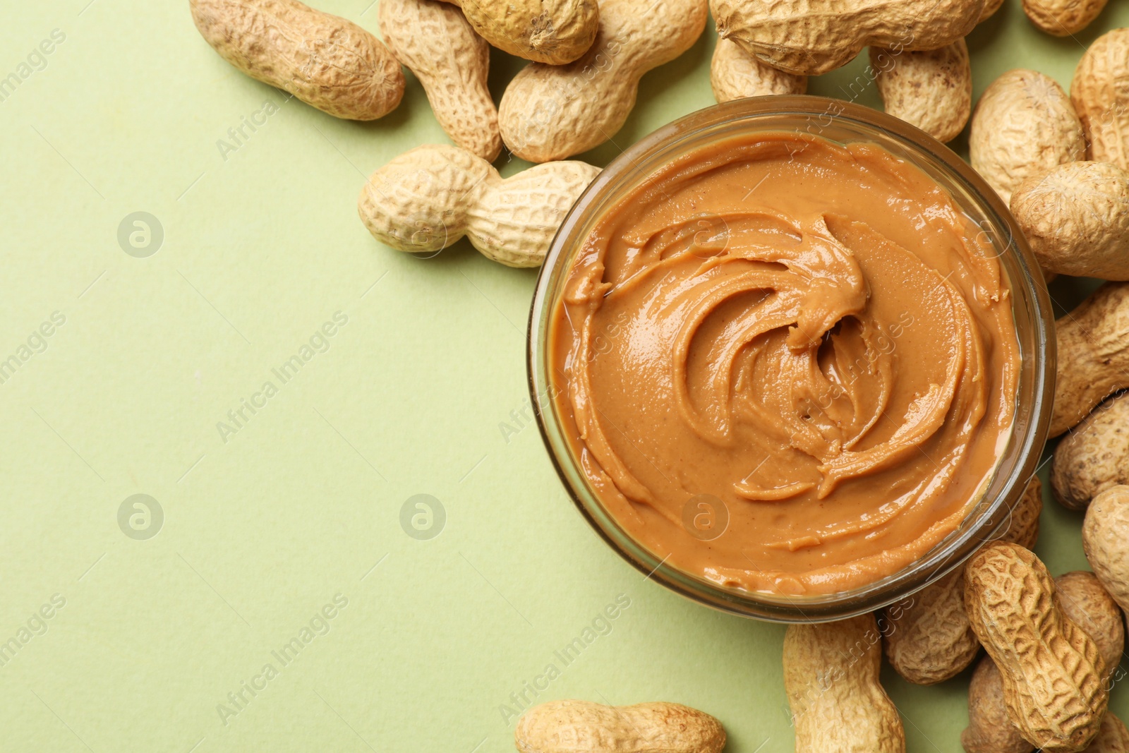 Photo of Tasty peanut butter in bowl and groundnuts on pistachio color background, flat lay. Space for text