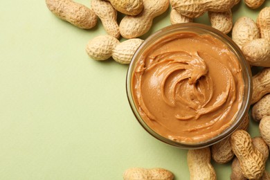 Photo of Tasty peanut butter in bowl and groundnuts on pistachio color background, flat lay. Space for text