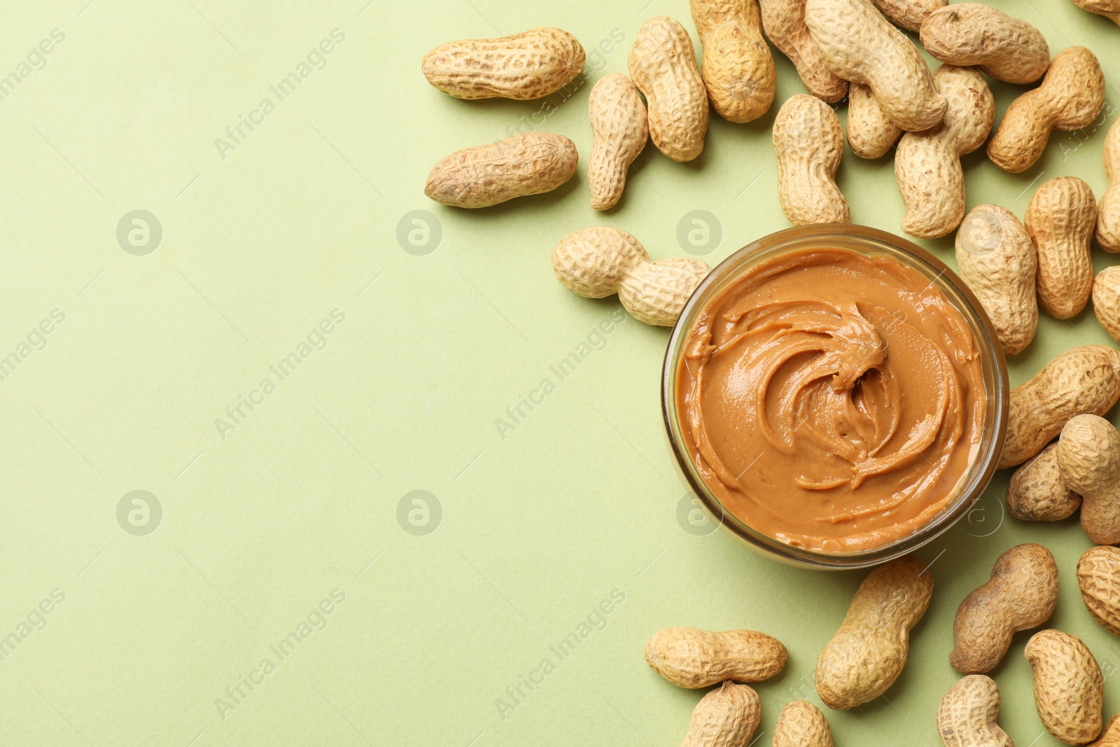 Photo of Tasty peanut butter in bowl and groundnuts on pistachio color background, flat lay. Space for text