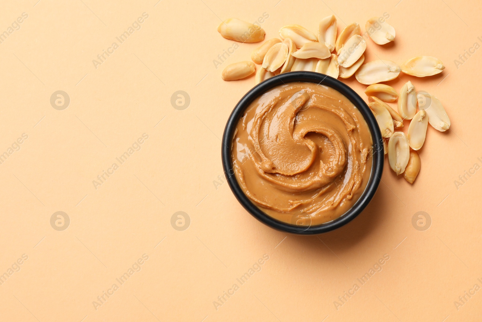 Photo of Tasty peanut butter in bowl and groundnuts on beige background, flat lay. Space for text