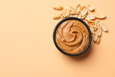 Tasty peanut butter in bowl and groundnuts on beige background, flat lay. Space for text