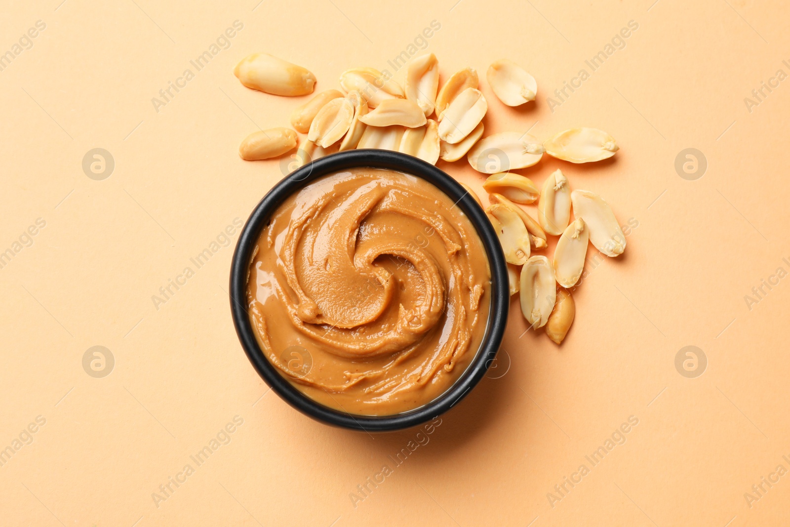 Photo of Tasty peanut butter in bowl and groundnuts on beige background, flat lay