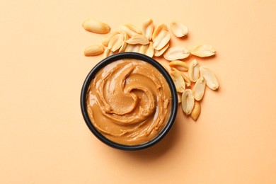 Photo of Tasty peanut butter in bowl and groundnuts on beige background, flat lay