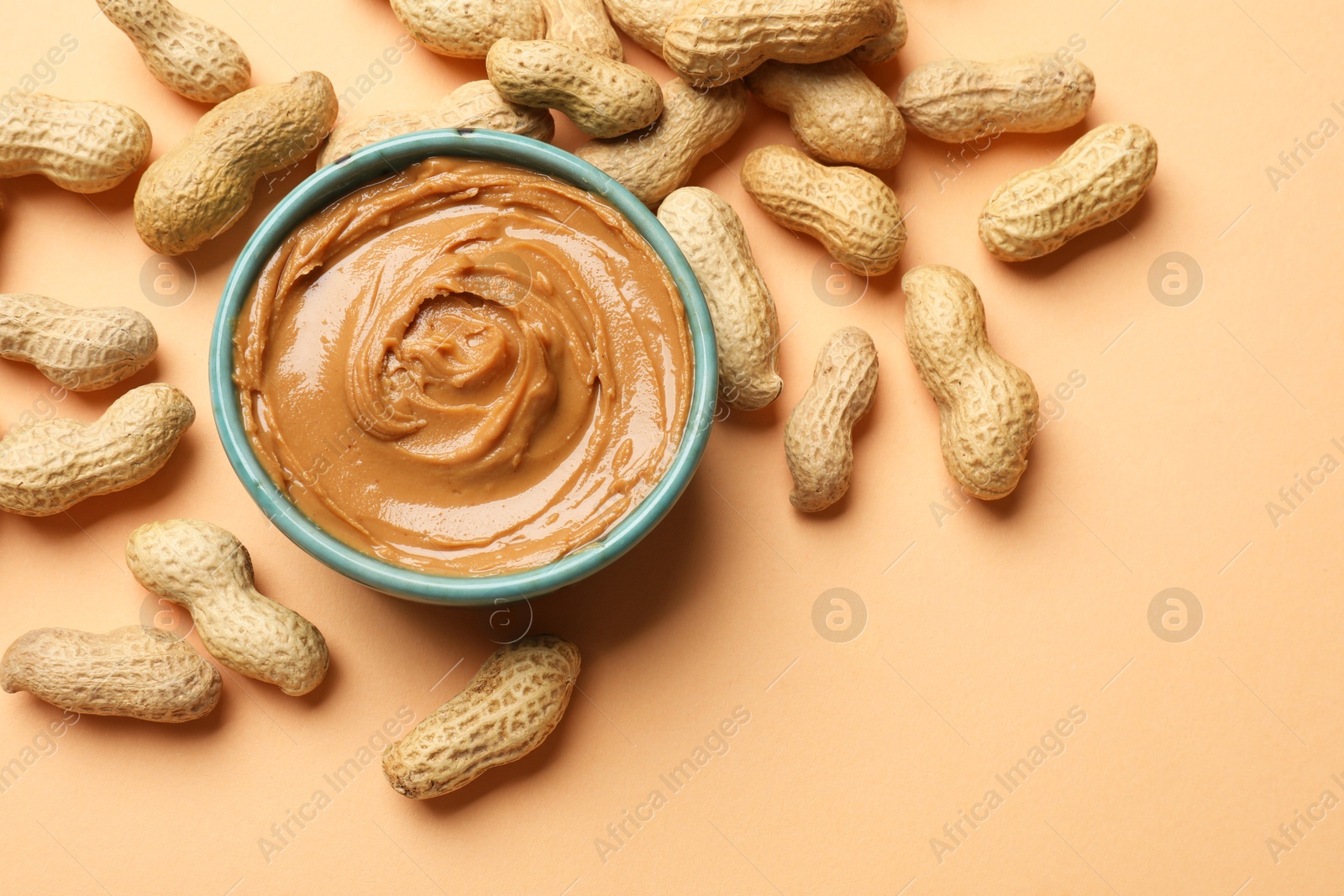 Photo of Tasty peanut butter in bowl and groundnuts on beige background, flat lay. Space for text