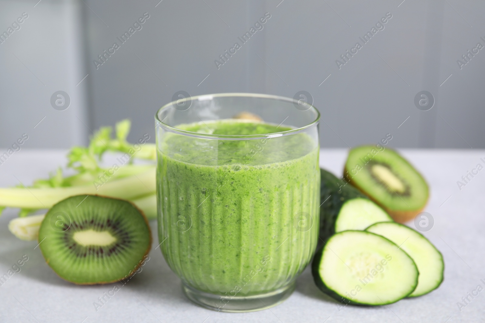 Photo of Delicious green smoothie and ingredients on light table, closeup