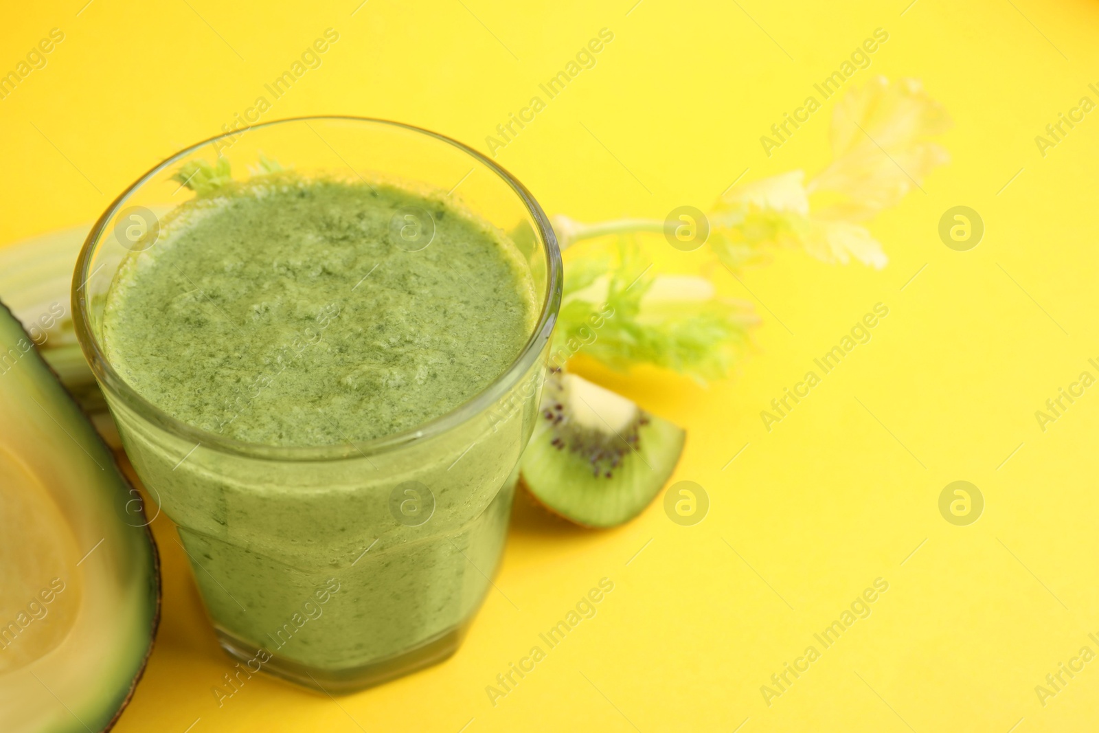 Photo of Delicious green smoothie and ingredients on yellow table, closeup. Space for text