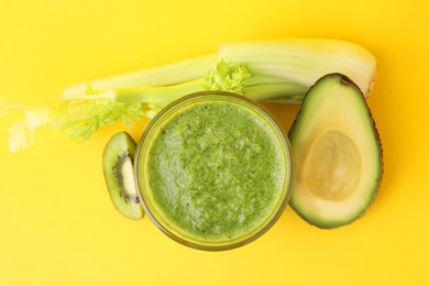 Photo of Delicious green smoothie and ingredients on yellow table, top view