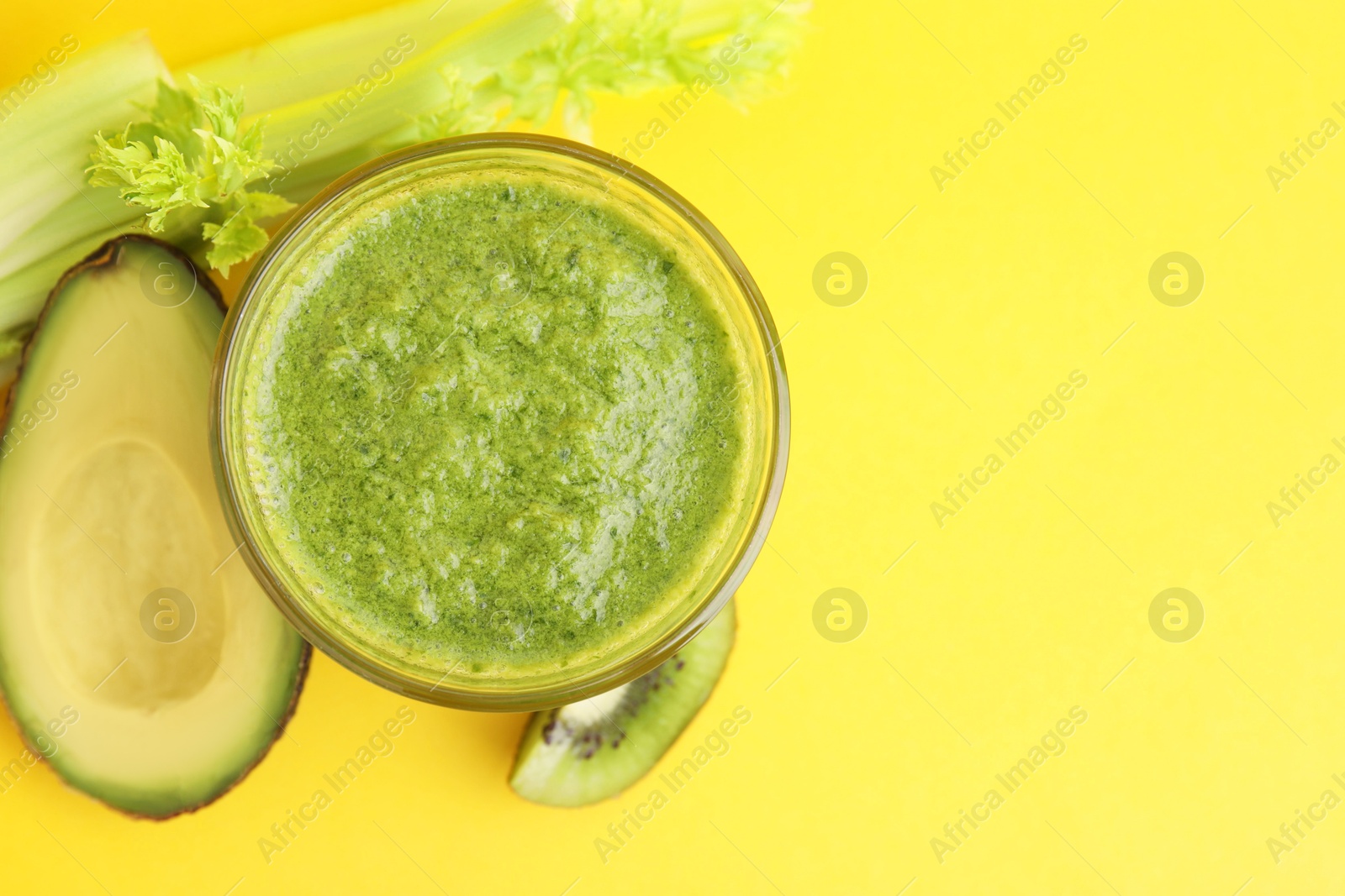 Photo of Delicious green smoothie and ingredients on yellow table, top view. Space for text