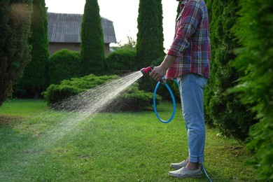 Photo of Man watering green grass on lawn in backyard, closeup