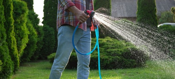 Photo of Man watering green grass on lawn in backyard, closeup