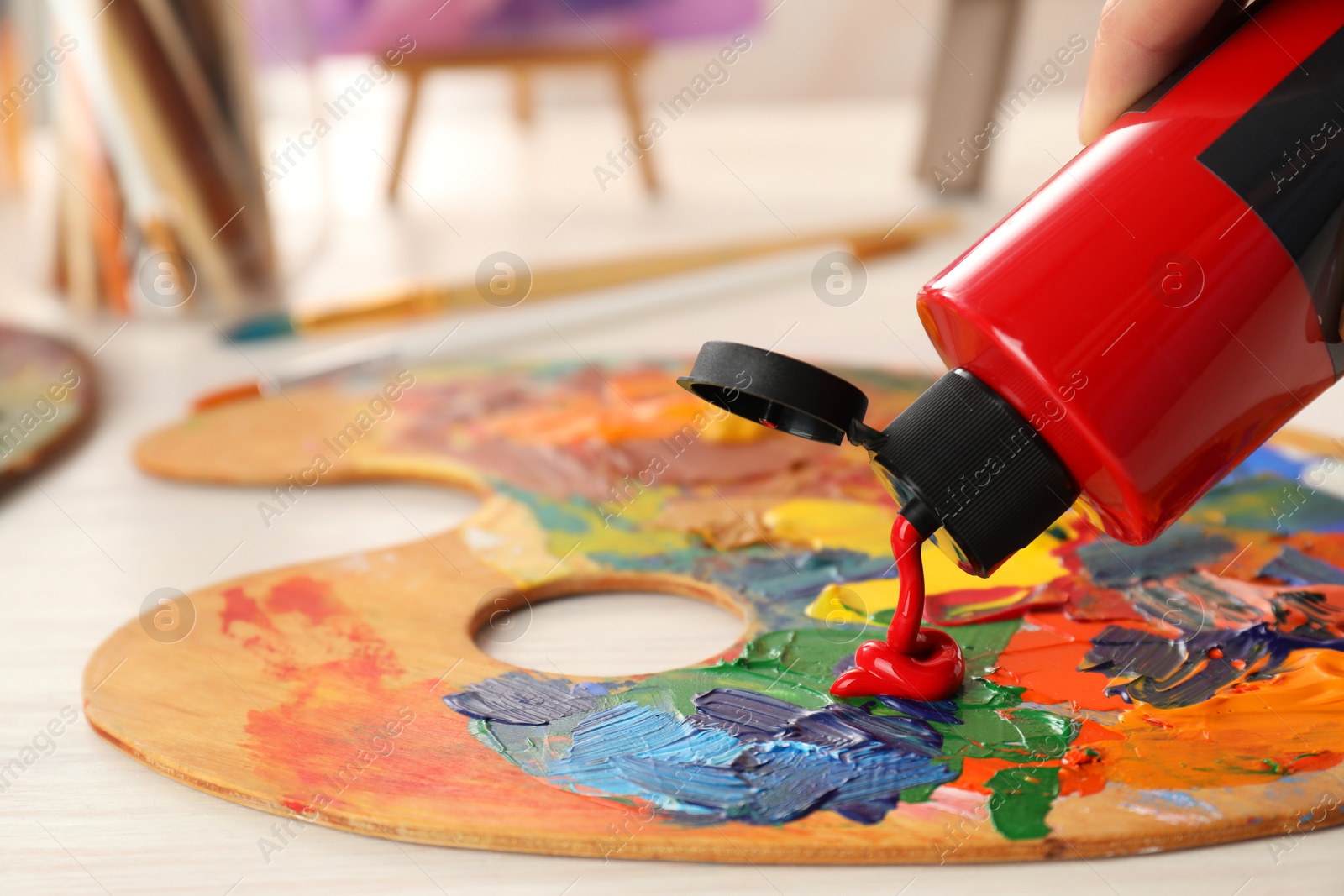 Photo of Squeezing red acrylic paint on palette at wooden table indoors, closeup