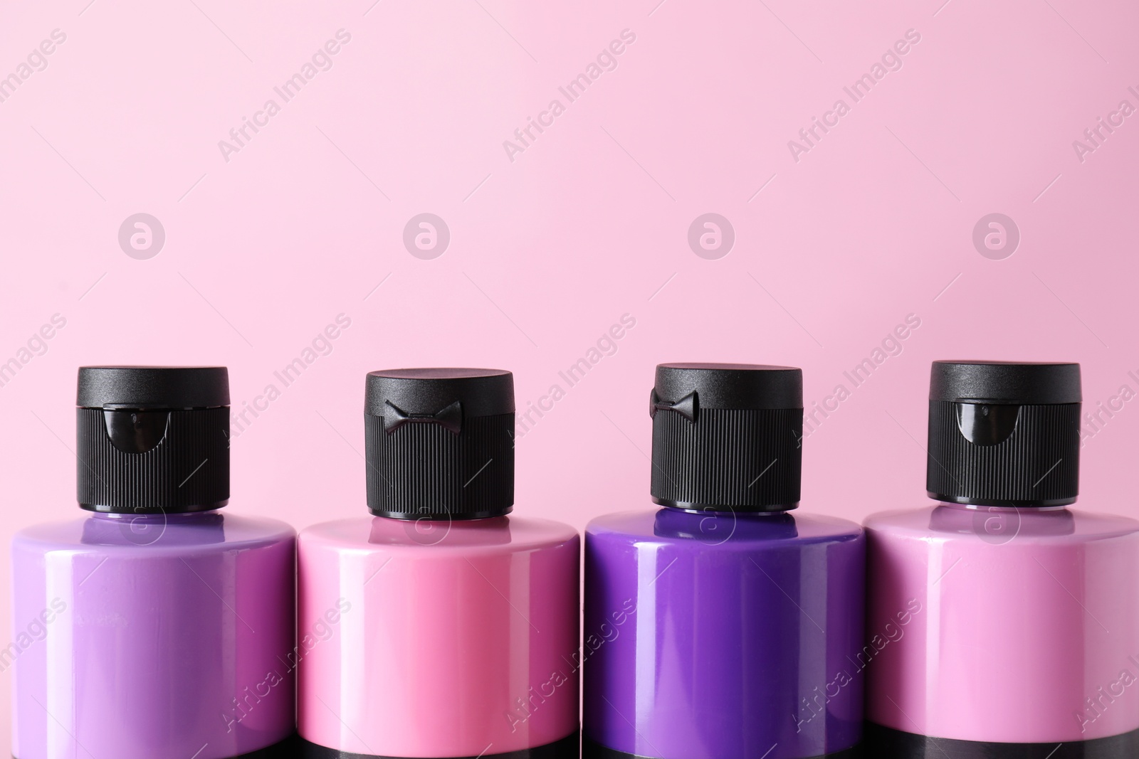 Photo of Acrylic paints of different colors on pink background, closeup