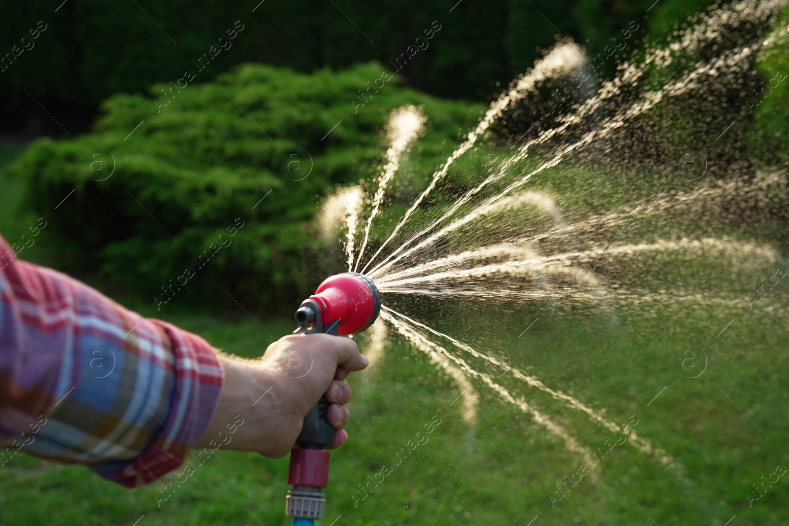 Photo of Man watering lawn with hose in backyard, closeup