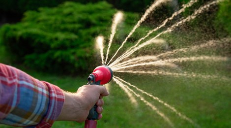 Photo of Man watering lawn with hose in backyard, closeup