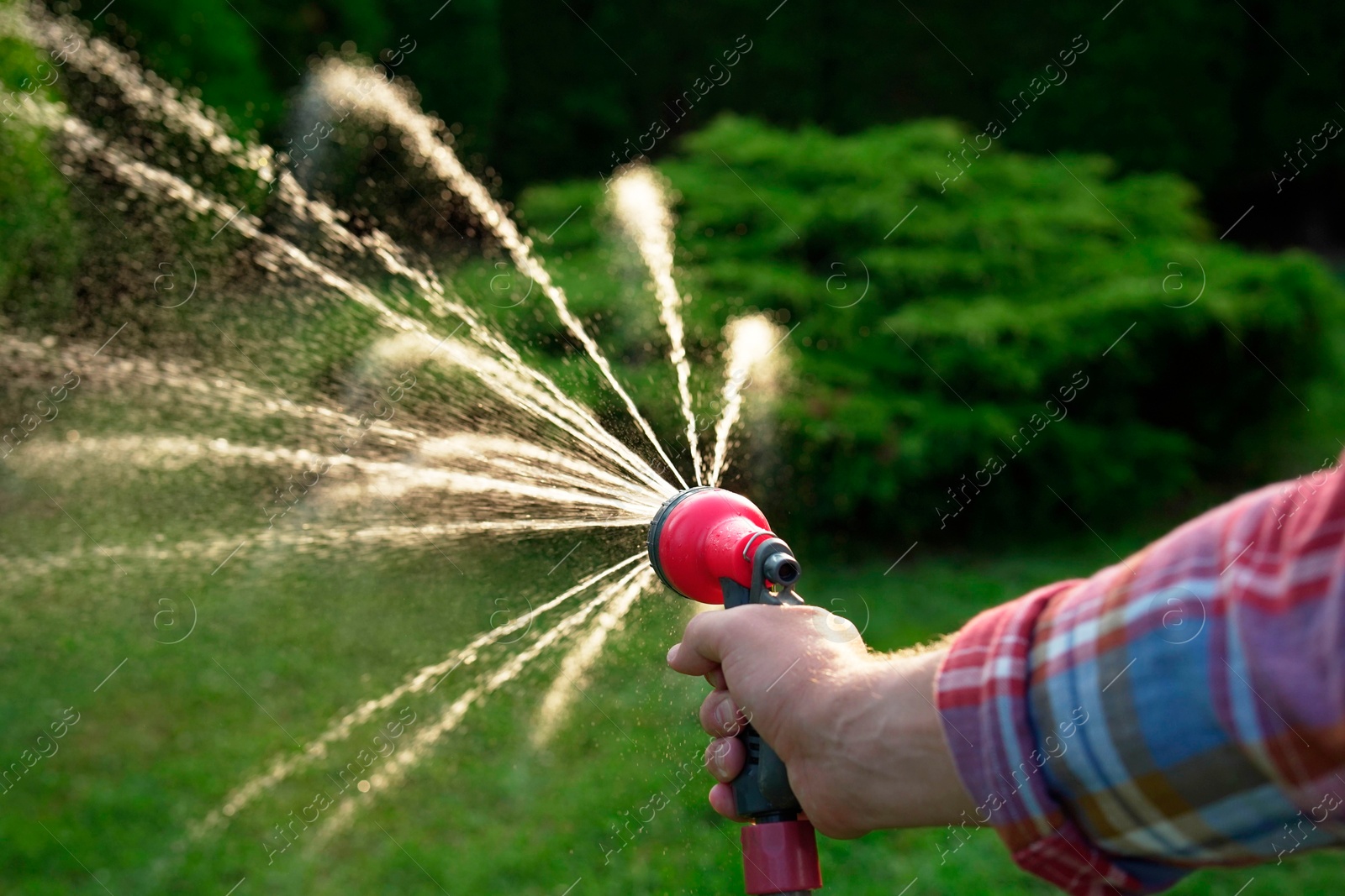 Photo of Man watering lawn with hose in backyard, closeup