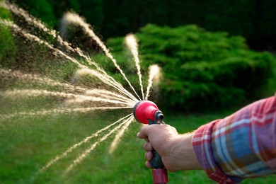 Photo of Man watering lawn with hose in backyard, closeup