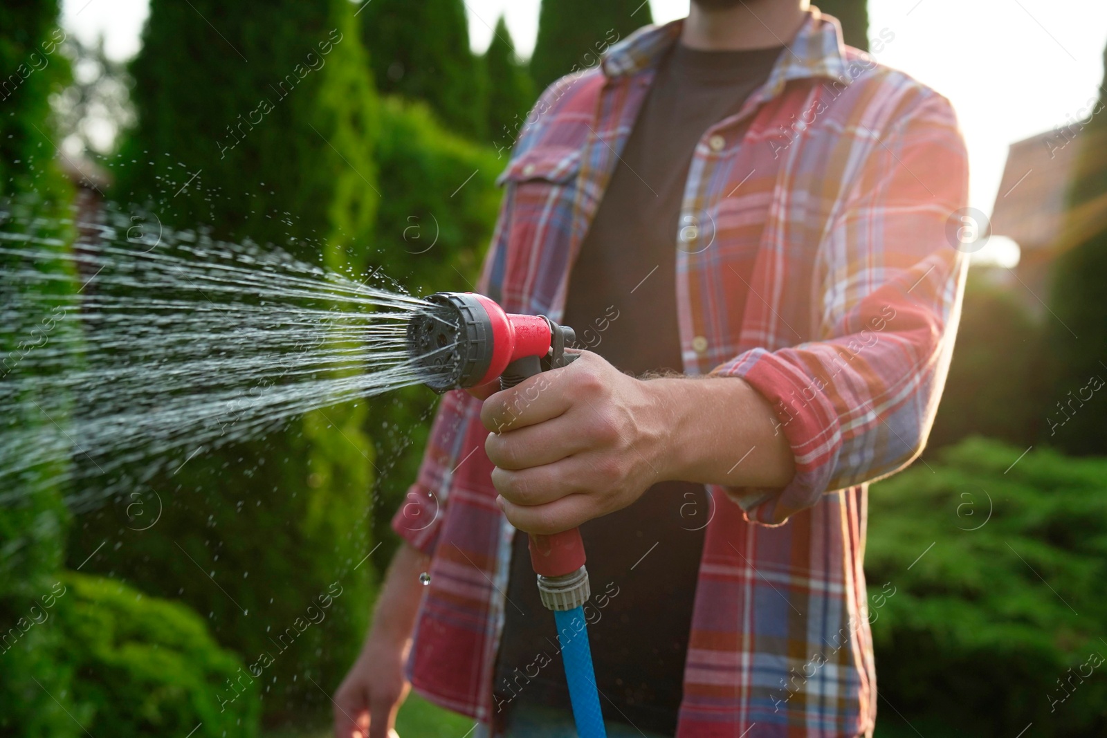 Photo of Man watering lawn with hose in backyard, closeup