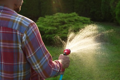 Man watering lawn with hose in backyard, closeup