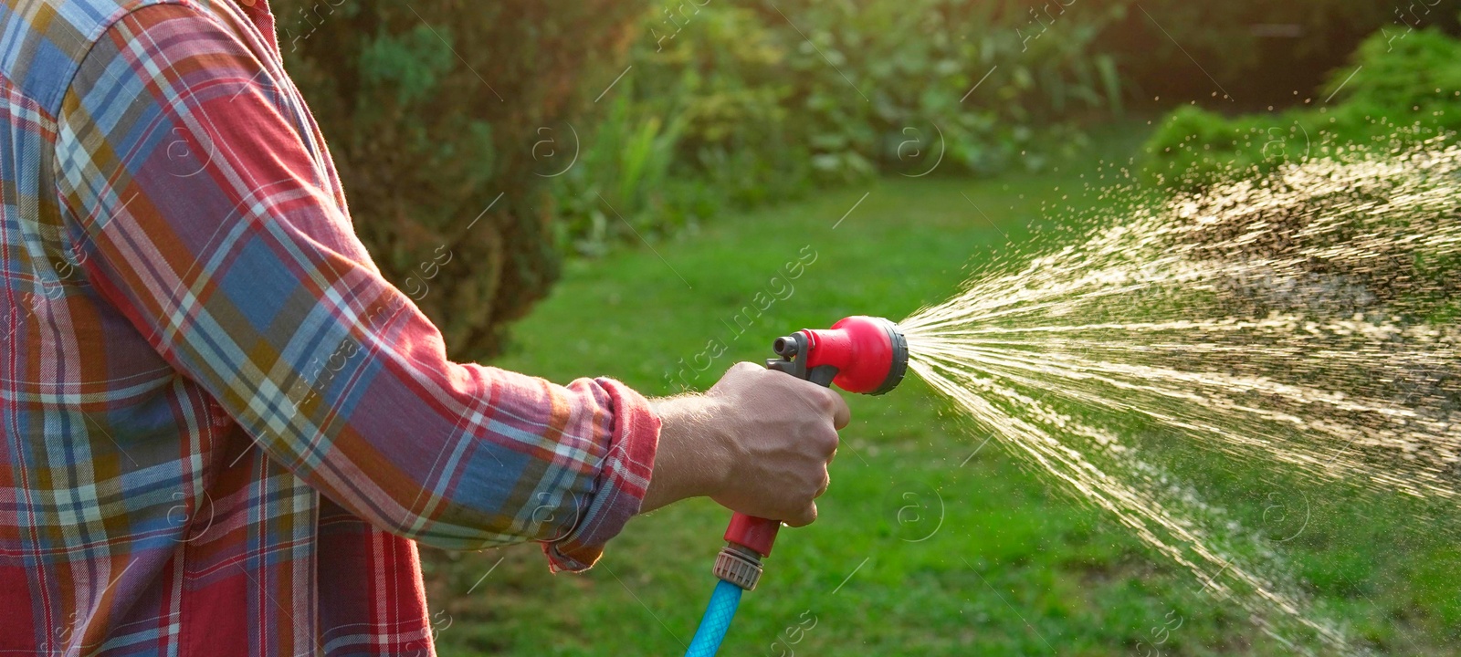 Photo of Man watering lawn with hose in backyard, closeup