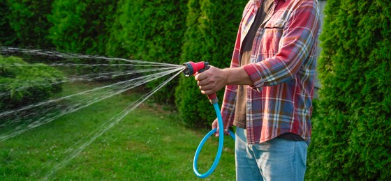 Photo of Man watering lawn with hose in backyard, closeup