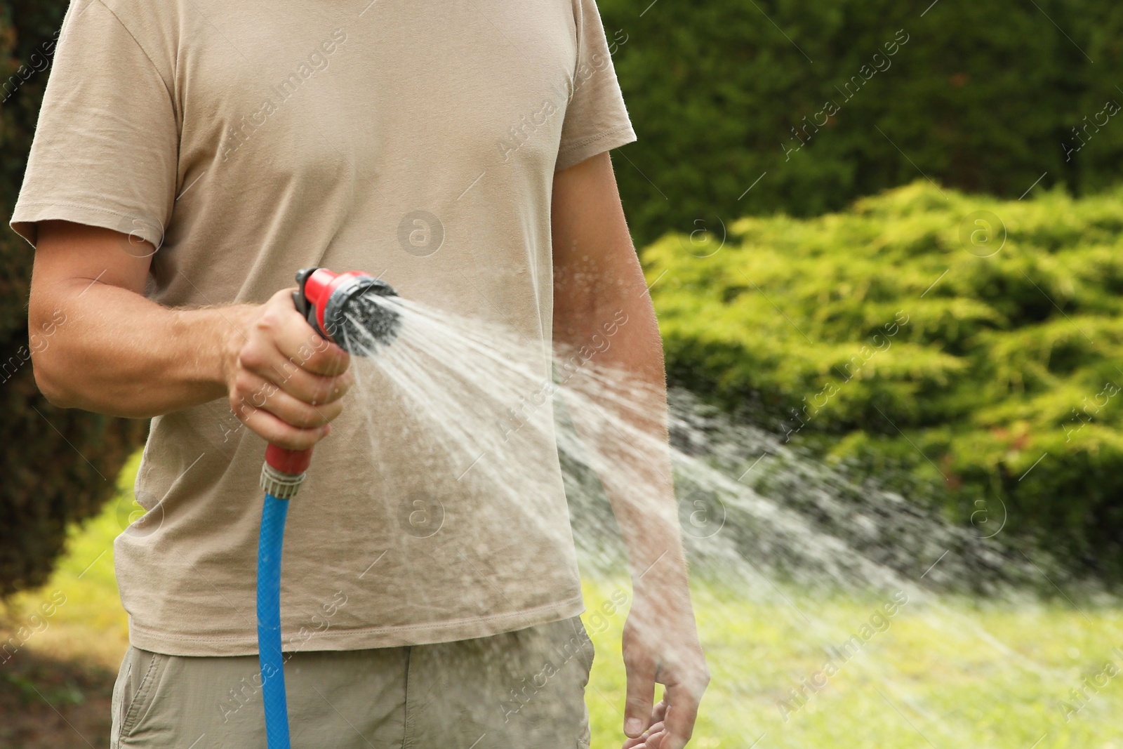 Photo of Man watering lawn with hose in backyard, closeup