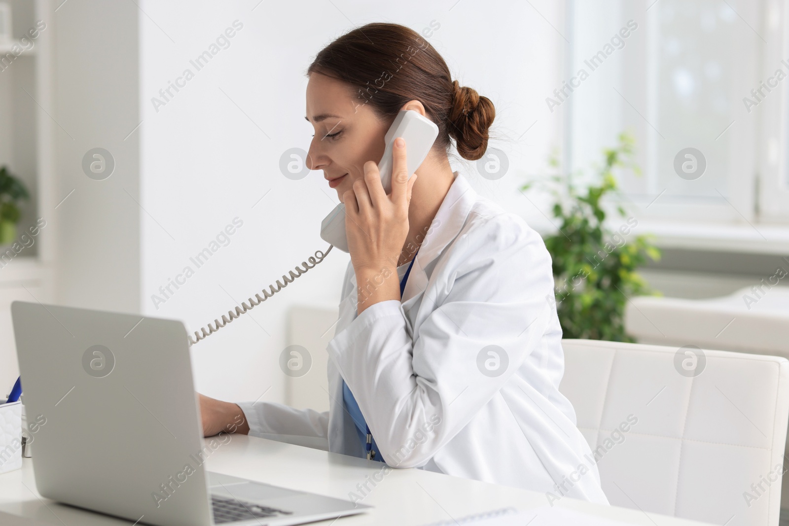 Photo of Nurse consulting patient by phone at white table in clinic