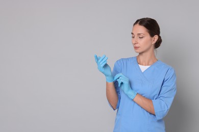 Nurse in medical uniform wearing gloves on grey background, space for text