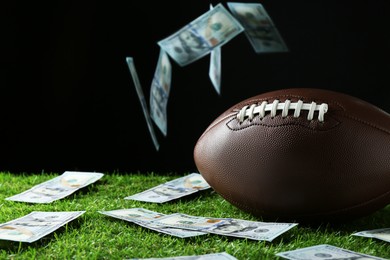 Photo of American football ball and dollar banknotes on green grass